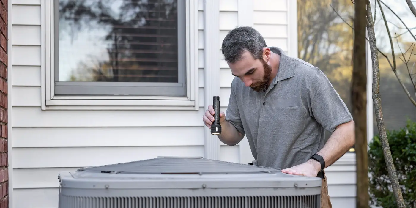 Technician inspecting an outdoor air conditioning unit beside a house